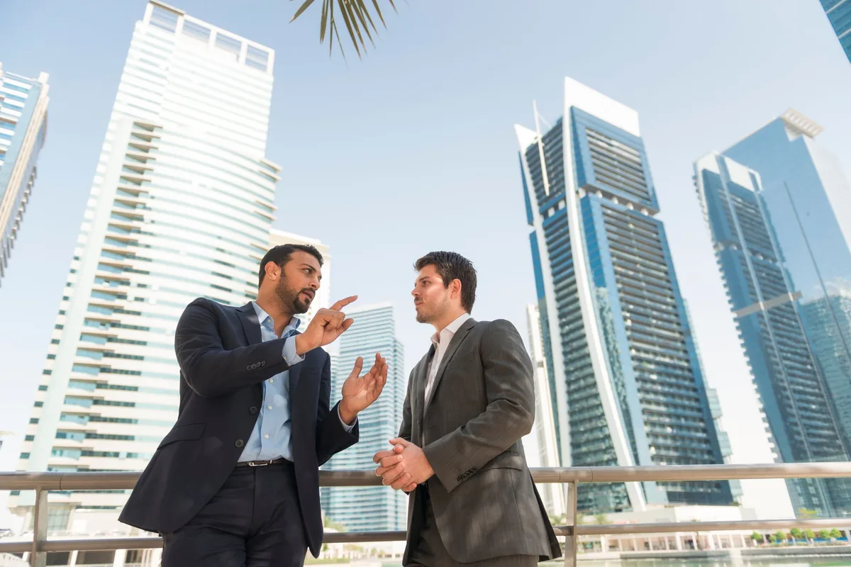 Zwei Geschäftsleute im Gespräch in Dubai, im Hintergrund die Skyline der Jumeirah Lakes Towers (JLT)