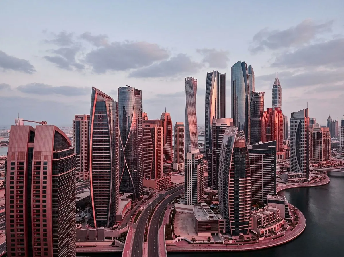 An aerial view of a modern city skyline with numerous skyscrapers reflecting the pink hues of sunset.