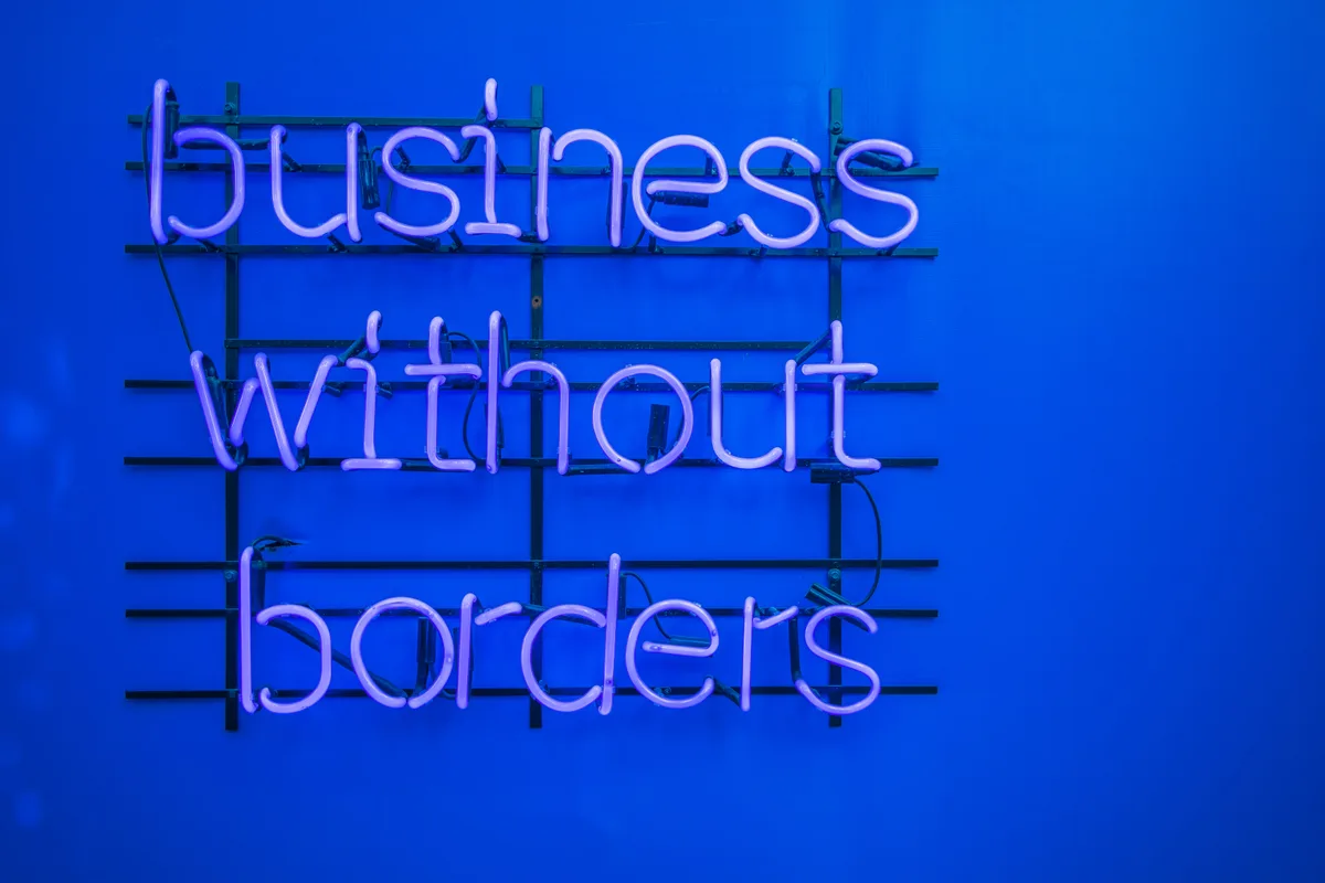 Ein Neonschild mit der Aufschrift „Business without Borders“ leuchtet lila vor einem leuchtend blauen Hintergrund und schafft eine moderne und kühne Atmosphäre.